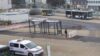 Busbahnhof mit Haltestelle, Bussen, Einsatzfahrzeug und Stadtgebäuden im Hintergrund.
