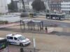 Busbahnhof mit Haltestelle, Bussen, Einsatzfahrzeug und Stadtgebäuden im Hintergrund.