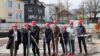 Eine Gruppe von acht Personen mit roten Bauhelmen und roten Spaten posiert auf einer Baustelle