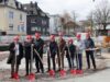Eine Gruppe von acht Personen mit roten Bauhelmen und roten Spaten posiert auf einer Baustelle