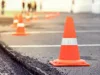 Mehrere orangefarbene Verkehrshütchen auf einem Asphaltplatz, im Hintergrund unscharfe Menschen.