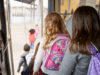 Gruppe von Schulkindern mit bunten Rucksäcken steigt aus einem Bus aus, Blick von hinten auf die Kinder.