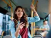 Weibliche Person steht im Bus, hält sich mit einer Hand an der Schlaufe fest und bedient mit der anderen ihr Smartphone