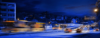 Langzeitbelichtetes Nachtfoto von einer Straße mit vorbeifahrenden Bussen und Autos, Lichter ziehen Leuchtspuren, im Hintergrund Wohnhäuser und Straßenschilder.