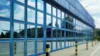 Große Fensterfront eines blauen Industriegebäudes mit Spiegelungen von Himmel und Umgebung.